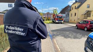 Ein Mann steht mit einer Jacke mit der Aufschrift "polizeilicher Brandermittler" vor einem abgebrannten Haus in Kirkel (Foto: SR / Jürgen Rinner)