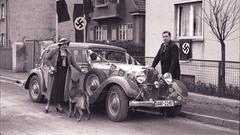 Ein Paar mit Schäferhund steht vor einem Auto, das mit Hakenkreuzfähnchen geschmückt ist. (Foto: Landesarchiv des Saarlandes/Julius Walter, Dudweiler)