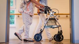 Eine Pflegekraft geht in einem Pflegeheim mit einer älteren Dame über einen Korridor (Foto: picture alliance/dpa | Christoph Schmidt)