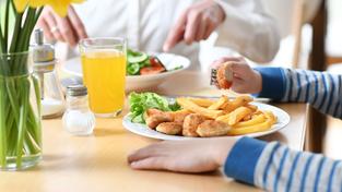 Ein Kind sitzt bei einer erwachsenen Person am Tisch beim Essen (Foto: picture alliance/dpa | Tobias Hase)