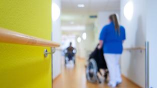 Eine Pflegerin schiebt einen Rollstuhl in einem Krankenhaus (Foto: dpa)