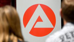 Zwei Personen stehen vor dem Logo der Agentur für Arbeit (Foto: picture alliance/dpa | Carsten Rehder)