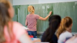 Eine junge Lehrerin schreibt an einer Schultafel. (Foto: picture alliance/dpa | Julian Stratenschulte)