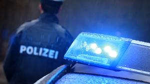 Ein Polizist steht im Regen vor einem Streifenwagen dessen Blaulicht aktiviert ist.  (Foto: picture alliance/dpa | Karl-Josef Hildenbrand)
