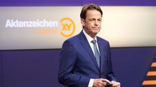ZDF-Moderator Rudi Cerne. Im Hintergrund das Logo der Sendung "Aktenzeichen xy ungelöst" (Foto: picture alliance/dpa | Annette Riedl)