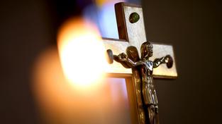 Eine Kerze vor einem Kreuz mit einer Jesusfigur (Foto: dpa)
