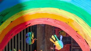 Illustration: Bunte Kinder-Handabdrücke unter einem Regenbogen sind an einem Fenster zu sehen (Foto: picture alliance/dpa/dpa-Zentralbild | Jens Kalaene)