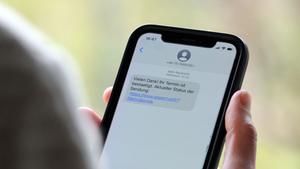 Eine Frau hält ein Smartphone in ihrer Hand, auf dessen Display eine Betrugs-SMS zu lesen ist (Foto: picture alliance/dpa | Wolf von Dewitz)
