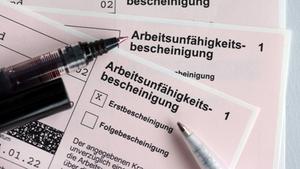 Stifte liegen auf Arbeitsunfähigkeitsbescheinigungen für Arbeitnehmer. (Foto: picture alliance/dpa/dpa-Zentralbild | Jens Büttner)