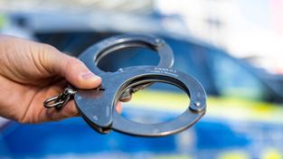 Eine Hand hält Handschellen vor einem Streifenwagen der Polizei (Foto: picture alliance/dpa | David Inderlied)