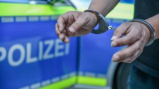Symbolbild Festnahme. Eine Person mit Handschellen vor einem Polizeifahrzeug (Foto: picture alliance / Ostalb Network | Marius Bulling)