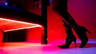 Eine Prostituierte mit Lackstiefeln steht vor einem Bett mit roter Unterbeleuchtung. (Foto: picture alliance/dpa | Hauke-Christian Dittrich)