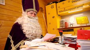 St. Nikolaus sitzt im Nikolauspostamt in St. Nikolaus vor vielen Briefen. (Foto: picture alliance/dpa/Festausschuss St. Nikolaus | --)