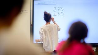 Ein Lehrerin schreibt Zahlen auf eine digitale Schultafel im Klassenraum  (Foto: picture alliance/dpa | Julian Stratenschulte)
