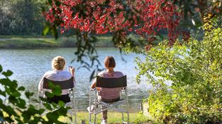Zwei Frauen sitzen auf Campingstühlen an einem See in der Sonne. (Foto: picture alliance/dpa | Thomas Warnack)