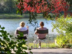Zwei Frauen sitzen auf Campingstühlen an einem See in der Sonne. (Foto: picture alliance/dpa | Thomas Warnack)