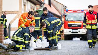 Einsatzkräfte der Feuerwehr mit Sandsäcken an einem Kanaldeckel (Foto: picture alliance/dpa | Moritz Frankenberg)