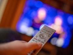 Ein Mann bedient mit der Fernbedienung einen Fernseher. (Foto: picture alliance/dpa | Lino Mirgeler)
