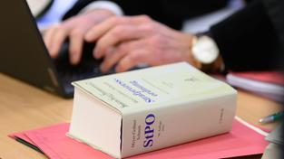 Ein dickes Buch mit der Aufschrift „Strafprozessordnung“ (StPO) liegt bei Gericht neben einem Anwalt (Foto: picture alliance/dpa | Swen Pförtner)