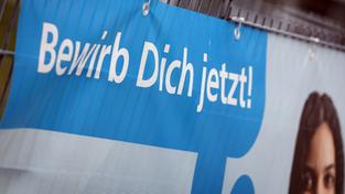 «Bewirb dich jetzt» ist auf einem Banner am Zaun einer Firma zu lesen (Foto: picture alliance/dpa | Karl-Josef Hildenbrand)