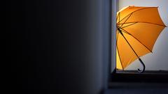 Ein gelber Regenschirm wird auf einem Büroflur durch eine offene Tür von der Sonne beleuchtet (Foto: picture alliance/Martin Gerten/dpa)