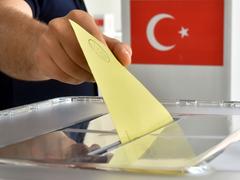 Ein Stimmzettel wird in einer Wahlurne eingeworfen, im Hintergrund eine türkische Staatsflagge (Foto: picture alliance / dpa | Uli Deck)