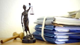 Akten mit der Statue der römischen Göttin Justitia, dem Symbol für die Rechtsprechung. (Foto: picture alliance / dpa | Volker Hartmann)
