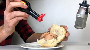 eine Person gibt Maggi auf ein Lyoner-Brötchen vor einem Mikrofon (Foto: SR)