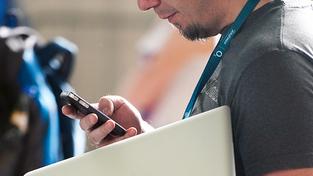 Ein Mann tippt auf einem Smartphone während er ein Laptop im Arm hält (Foto: dpa)