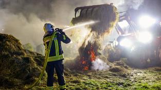 Heuballen werden mit einem Traktor auseinandergezogen um Glutnester im Inneren zu Löschen (Foto: Brandon Lee Posse)
