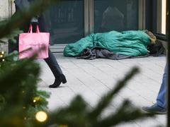 Passanten gehen mit Einkaufstüten in einer Fußgängerzone in der Innenstadt an einem schlafenden Obdachlosen vorbei. (Foto: IMAGO / Nikito)