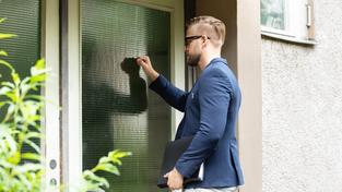 Symbolbild. Ein Mann mit Aktetasche klopft an die Eingangstür eines Hauses. (Foto: IMAGO / Panthermedia)