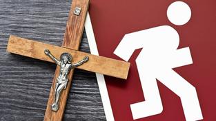 Symbolbild Kirchenaustritt. Ein Kreuz mit einem Notausgangsschild. (Foto: IMAGO / Christian Ohde)