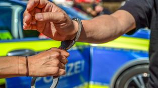 Ein Polizist legt einem Mann vor dem Einsatzwagen Handschellen an (Foto: IMAGO / onw-images)