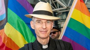 Der katholische Priester Wolfgang Rothe vor zwei Regenbogenflaggen. (Foto: IMAGO / Wolfgang Maria Weber)