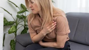 Eine Frau sitzt gebückt mit Schmerzen auf dem Sofa (Foto: IMAGO / Pond5 Images)