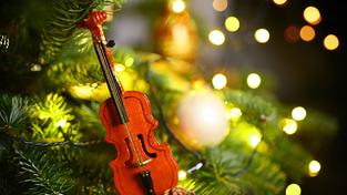 Eine kleine Violine hängt zwischen Deko und Lichtern an einem Weihnachtsbaum (Foto: IMAGO / Christian Ohde)