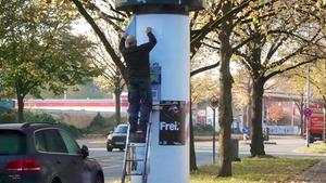 Ein Reklame-Kleber steht auf einer Leiter an einer Litfaßsäule und hängt Plakate auf (Foto: IMAGO / Rust)
