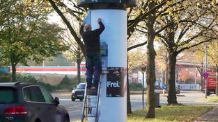 Ein Reklame-Kleber steht auf einer Leiter an einer Litfaßsäule und hängt Plakate auf (Foto: IMAGO / Rust)