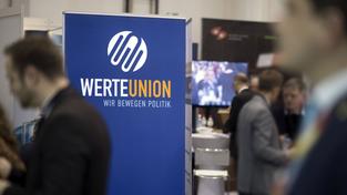 Werbeaufsteller mit dem Logo der „Werteunion“ steht zwischen mehreren Menschen (Foto: IMAGO / IPON)