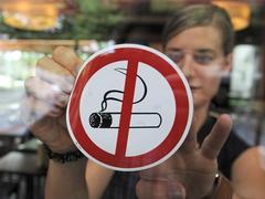 Eine Frau befestigt einen «Rauchen-Verboten»-Aufkleber an der Scheibe eines Cafes. (Foto: picture alliance / dpa | Armin Weigel)