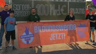 Bildungsprotest 2023. Lehrer und Schüler stehen mit einem Transparent "Bildungswende jetzt!" vor einer großen Schultafel auf einem Platz. (Foto: Christian von Polentz / transitfoto.de)