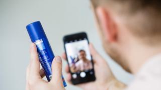 Ein Mann hält eine Sprayflasche in den Händen und filmt sich mit seinem Smartphone. (Foto: picture alliance / photothek | Thomas Trutschel)