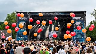 Orangene und rote Luftballons fliegen über dem Publikum. Im Hintergrund ist eine Bühne zu sehen. (Foto: Dirk Guldner)