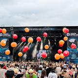 Orangene und rote Luftballons fliegen über dem Publikum. Im Hintergrund ist eine Bühne zu sehen. (Foto: Dirk Guldner)