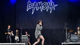 Eine Frau singt, im Hintergrund ist die Band und der Schriftzug "Damona" zu sehen. (Foto: Dirk Guldner)