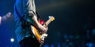 Ein Mann steht auf einer Bühne vor Publikum und spielt Gitarre  (Foto: pixabay.com)