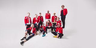 Alle elf Bandmitglieder stehen oder sitzen in roter Jacke im klassischen Marching Band-Look vor weißem Hintergrund. (Foto: Atelier (Presse))